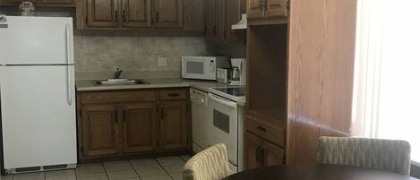 A kitchen with wooden cabinets, a white refrigerator, a microwave, and a dining table with chairs.
