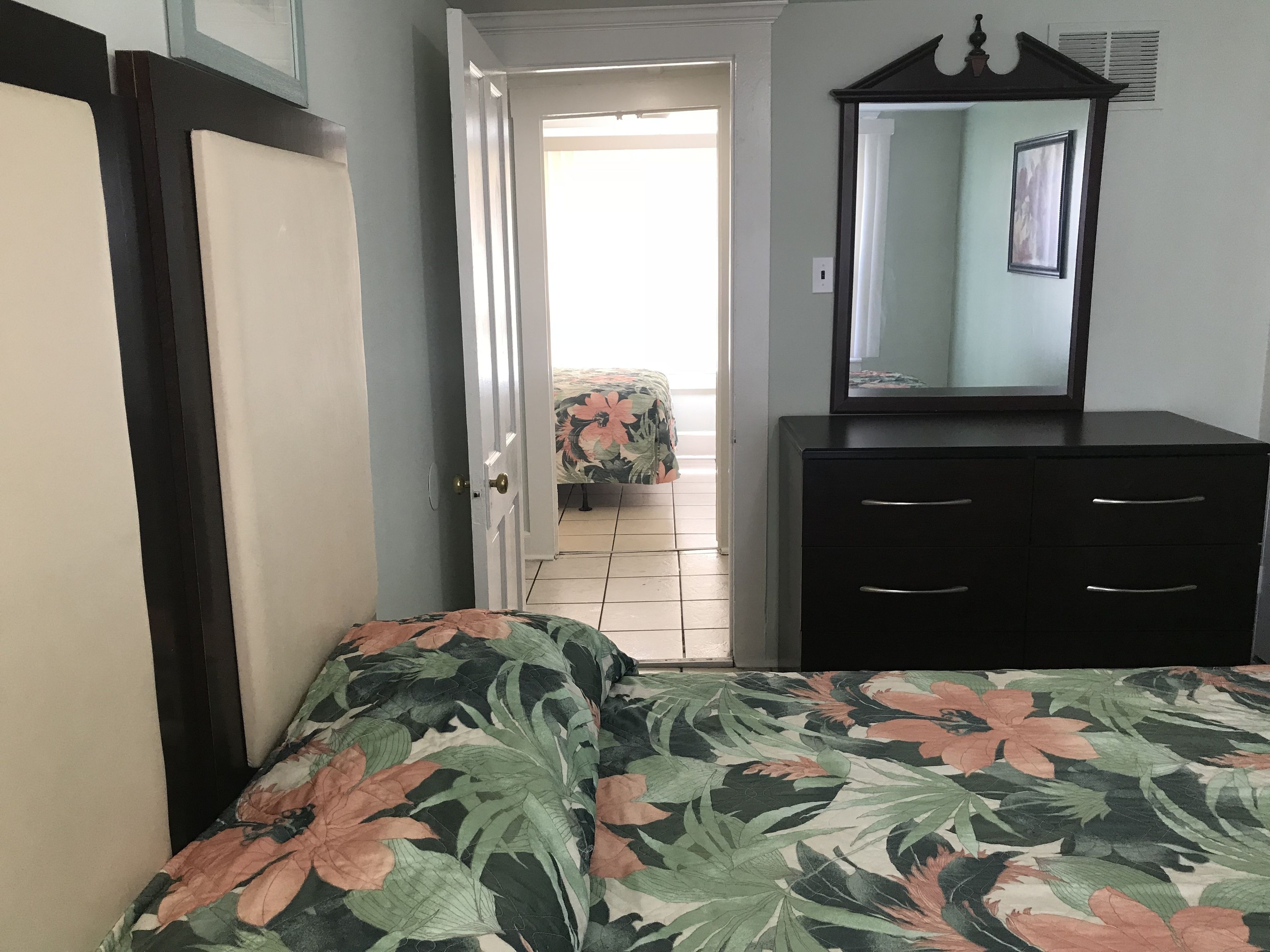 Un dormitorio con cama, cómoda y puerta que da a otra habitación.