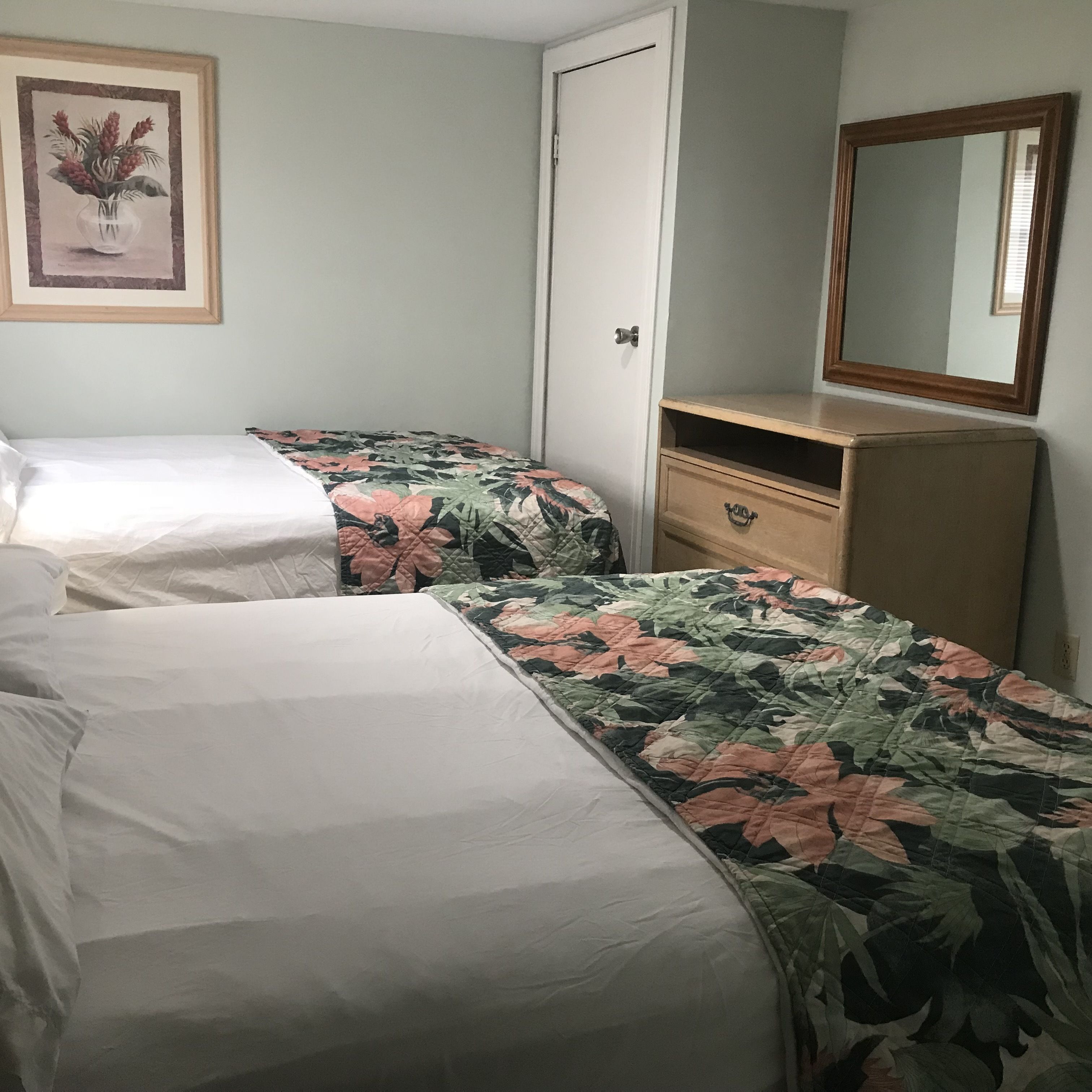 A bedroom with two single beds, a wooden dresser, a mirror, and a framed picture on the wall.