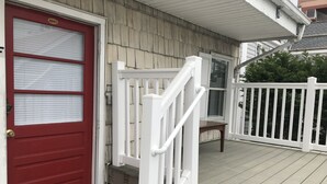 Una terraza de madera con una puerta roja y barandillas blancas.