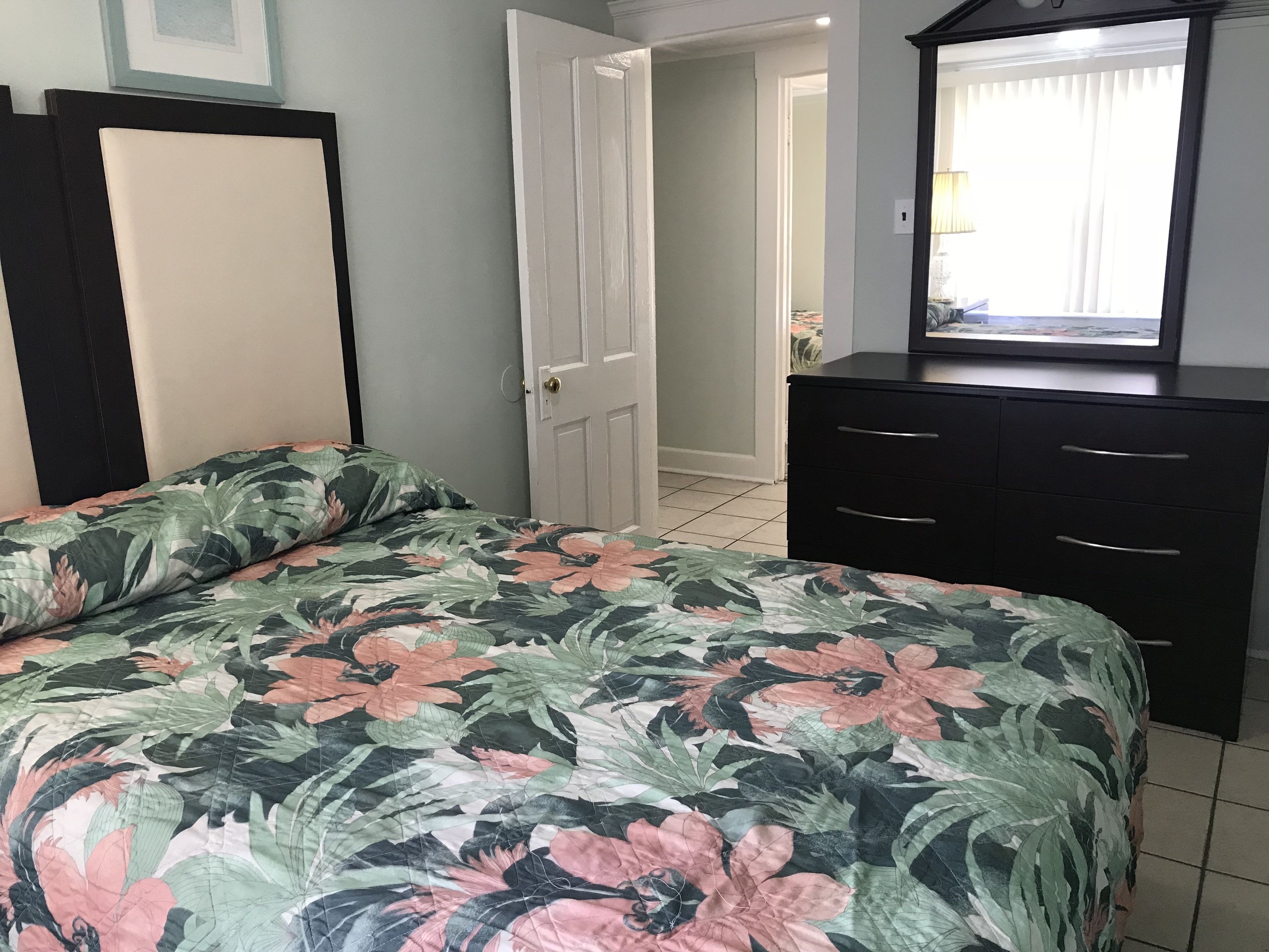 Un dormitorio con colcha estampada de flores, un aparador negro con cajones y una puerta blanca.