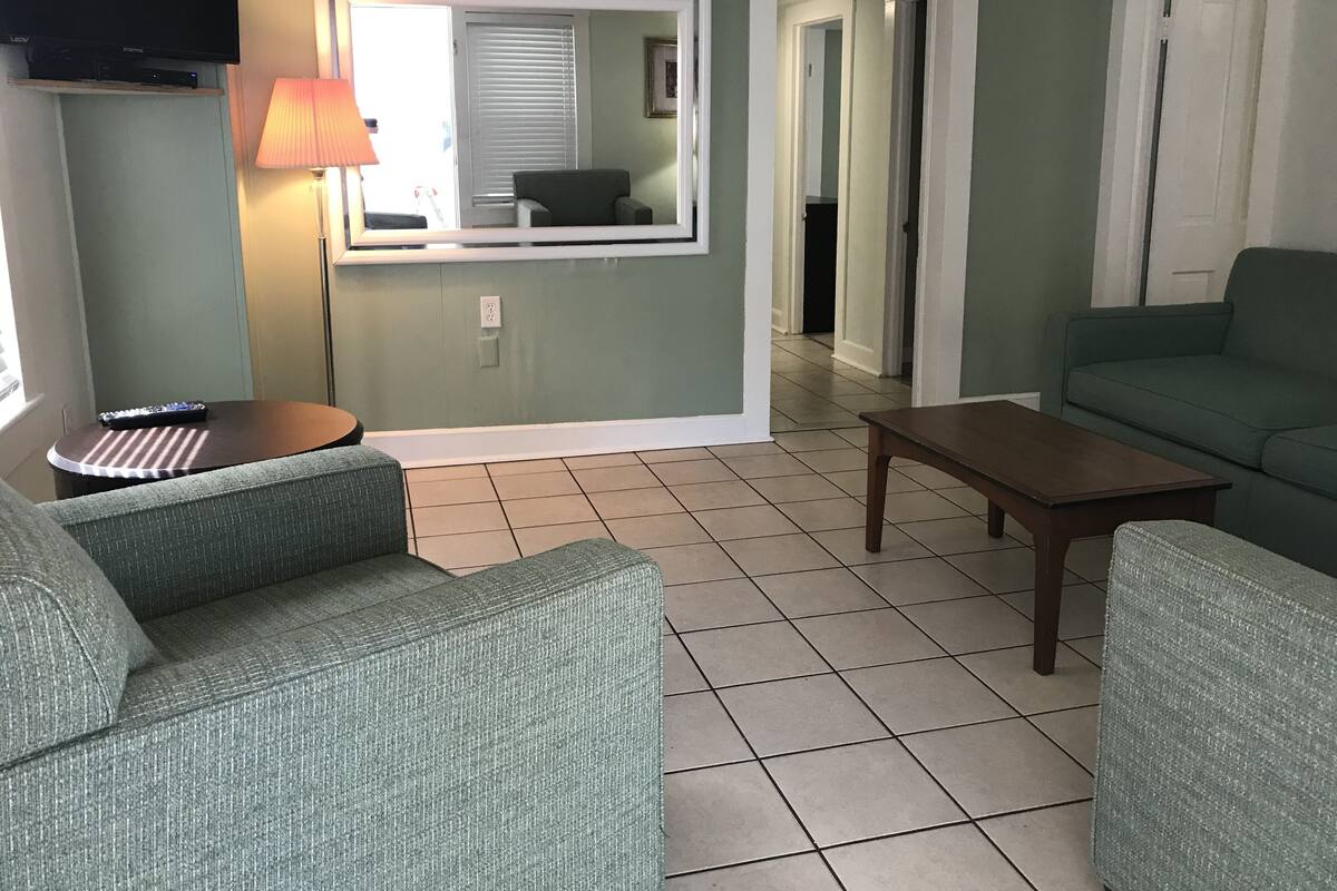 Una sala de estar con un sofá, una mesa de centro, un televisor sobre un mueble bajo y una lámpara.