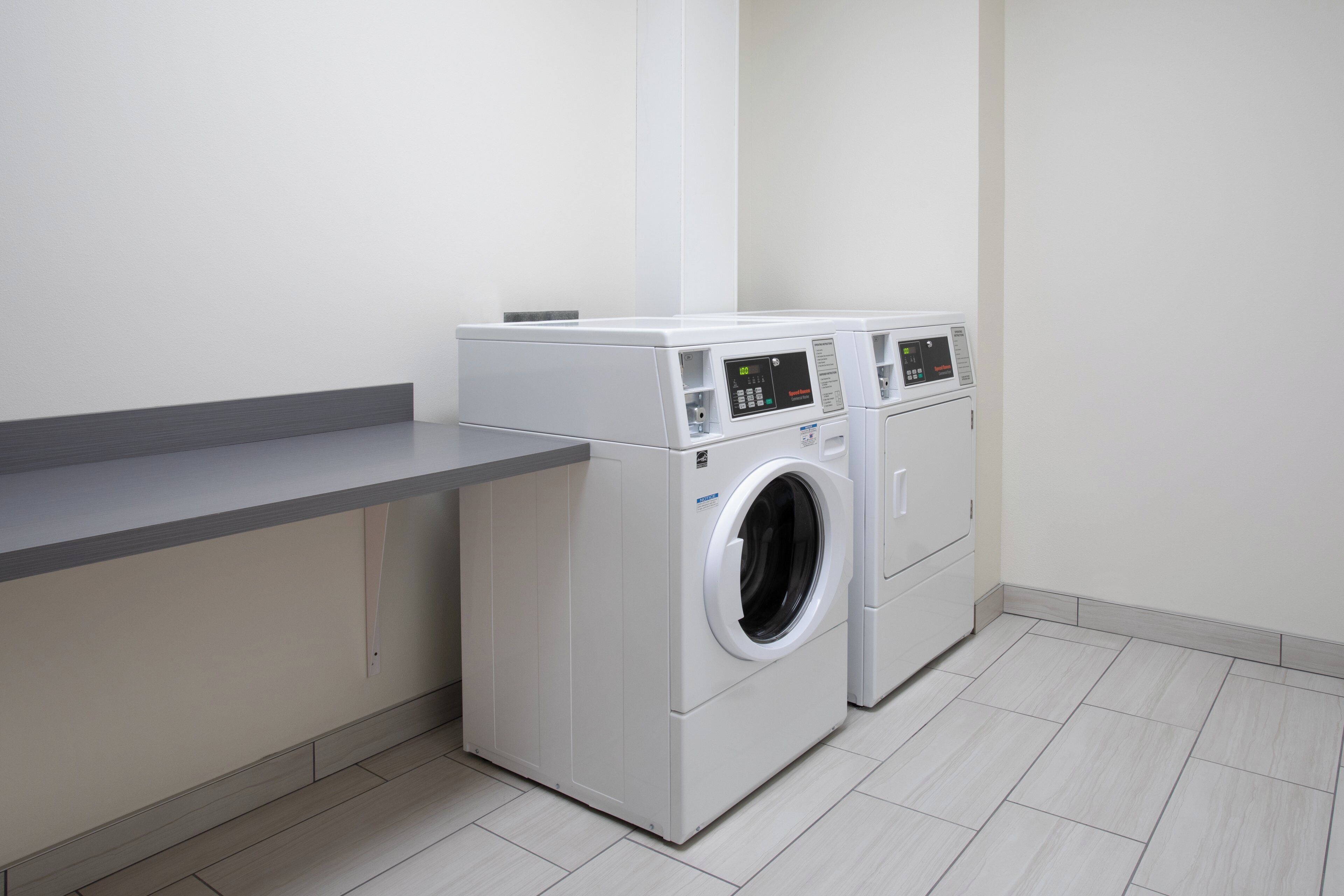 Une buanderie équipée de deux machines à laver à chargement frontal et d’un plan de travail gris.