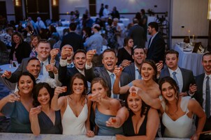 Um grupo de pessoas em um evento social em um espaço amplo e interno, com mesas e cadeiras dispostas para refeições ou convívio.