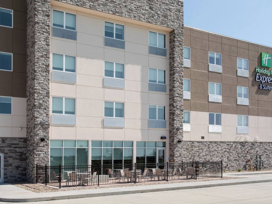 Edifício Holiday Inn Express & Suites com fachada de pedra, diversas janelas e área externa com mesas cercada por grades.