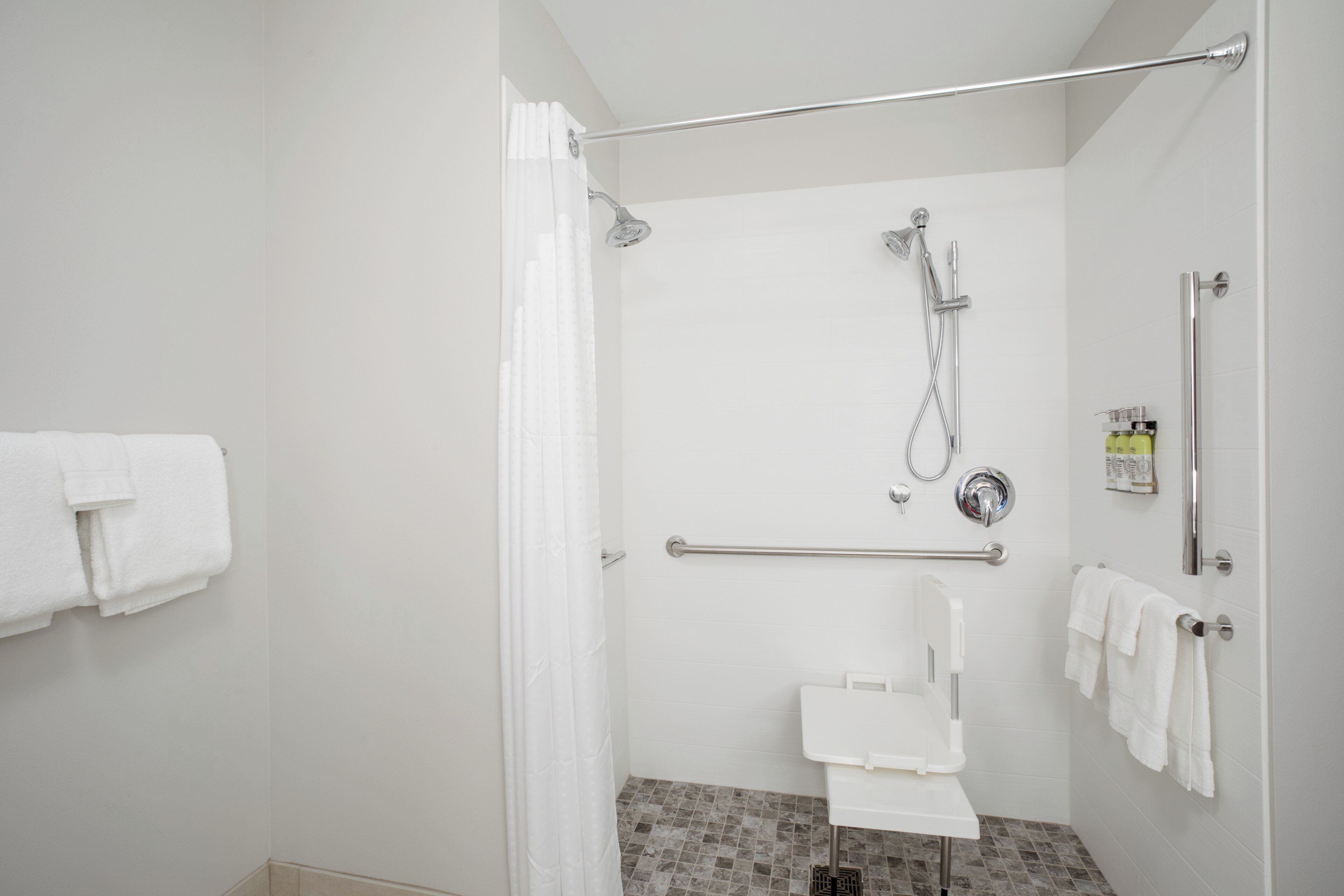 A bathroom with a shower, toilet, and handrails.