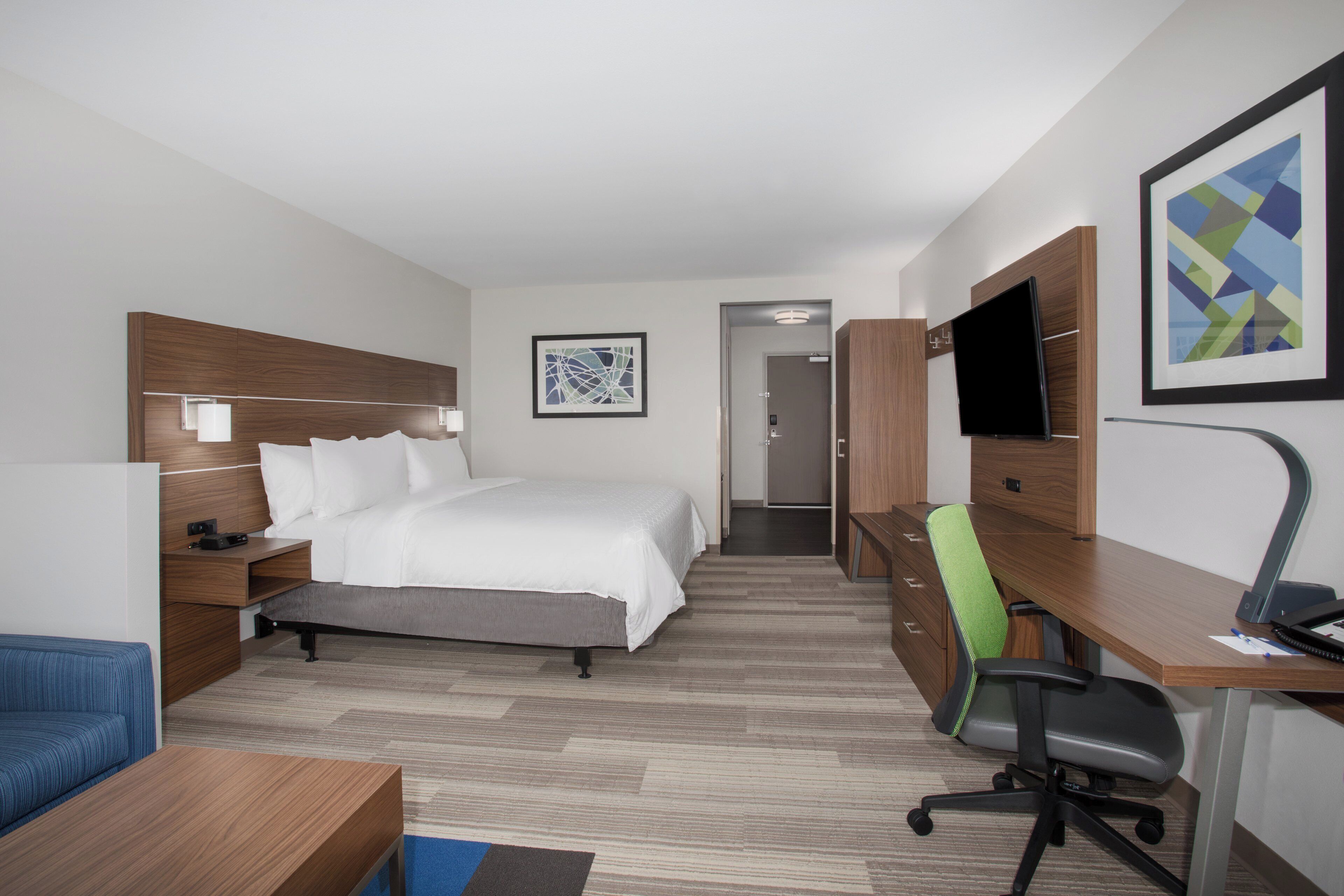 Ein Hotelzimmer mit Bett, Schreibtisch, Stuhl, Fernseher und einem gerahmten Bild an der Wand.