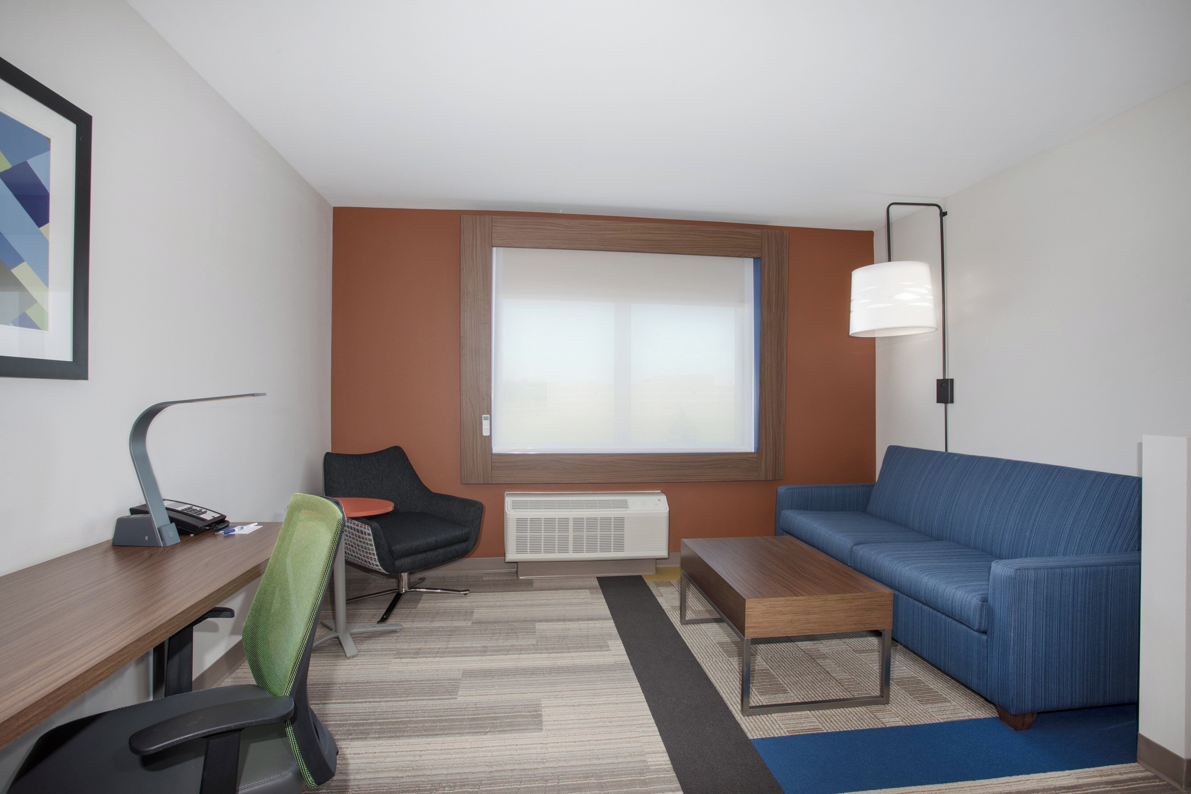 Una habitación de hotel moderna con escritorio, silla, sofá y un ventanal grande.
