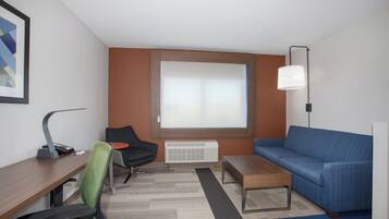 Una habitación de hotel moderna con escritorio, silla, sofá y un ventanal grande.