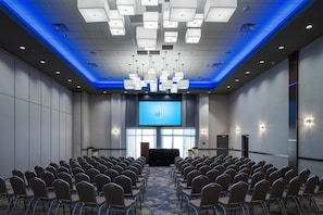 A conference room with rows of chairs facing a large screen, a podium, and a blue-lit ceiling. - Holiday Inn Express & Suites Sioux City North-Event Center by IHG (North Sioux City)