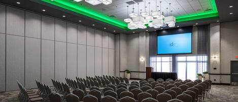 A conference room with rows of chairs, a large screen, and a podium.