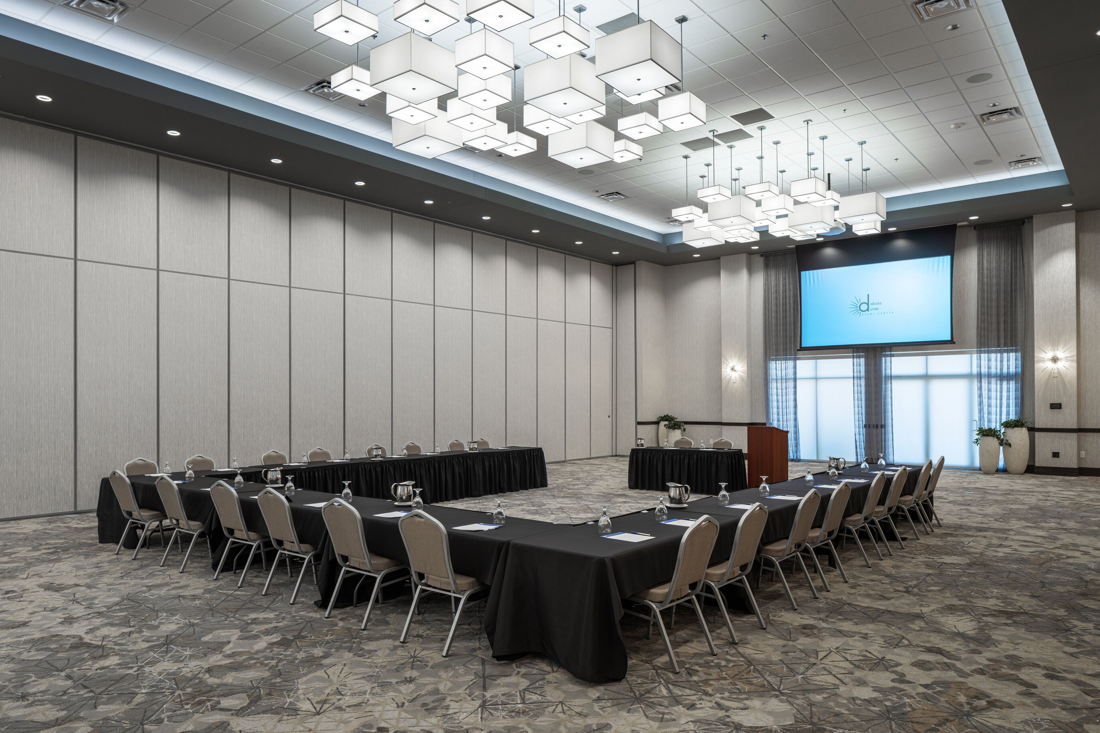 A conference room with a long table, chairs, a projector screen, and a podium.