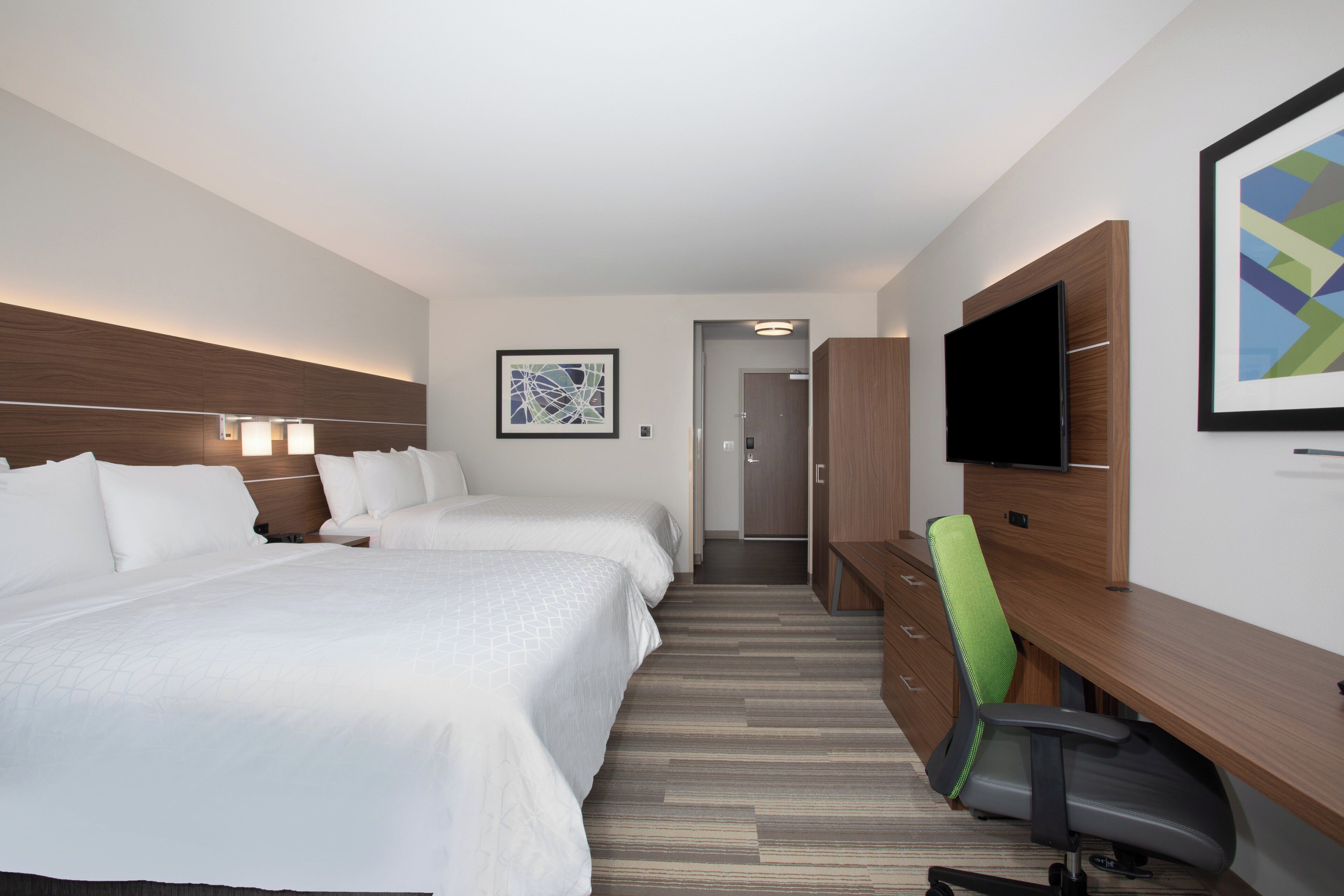 Een hotelkamer met twee bedden, een bureau met stoel, een televisie en kunst aan de muren.