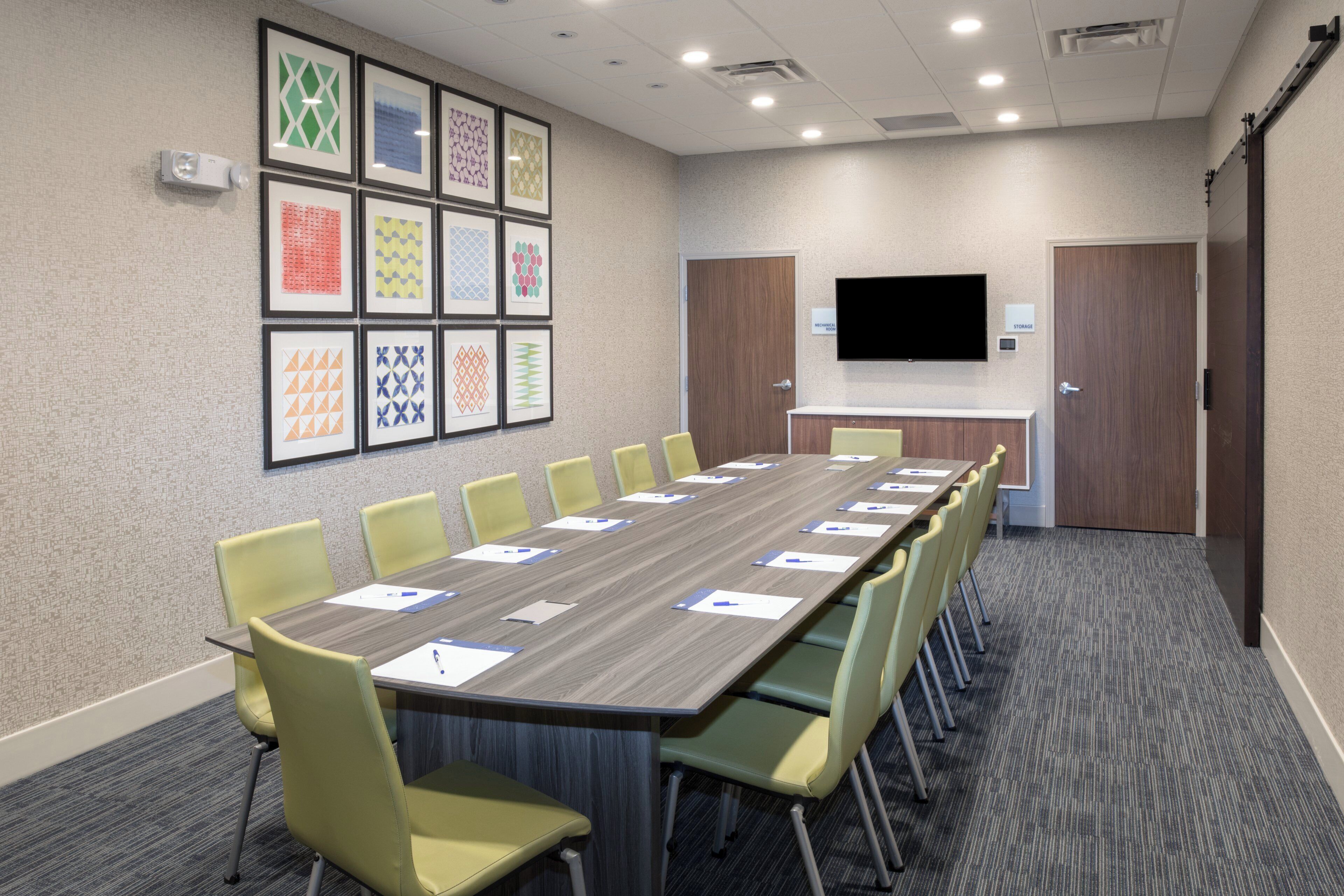 A conference room with a long table, multiple chairs, a flat-screen TV, and framed artwork on the wall.