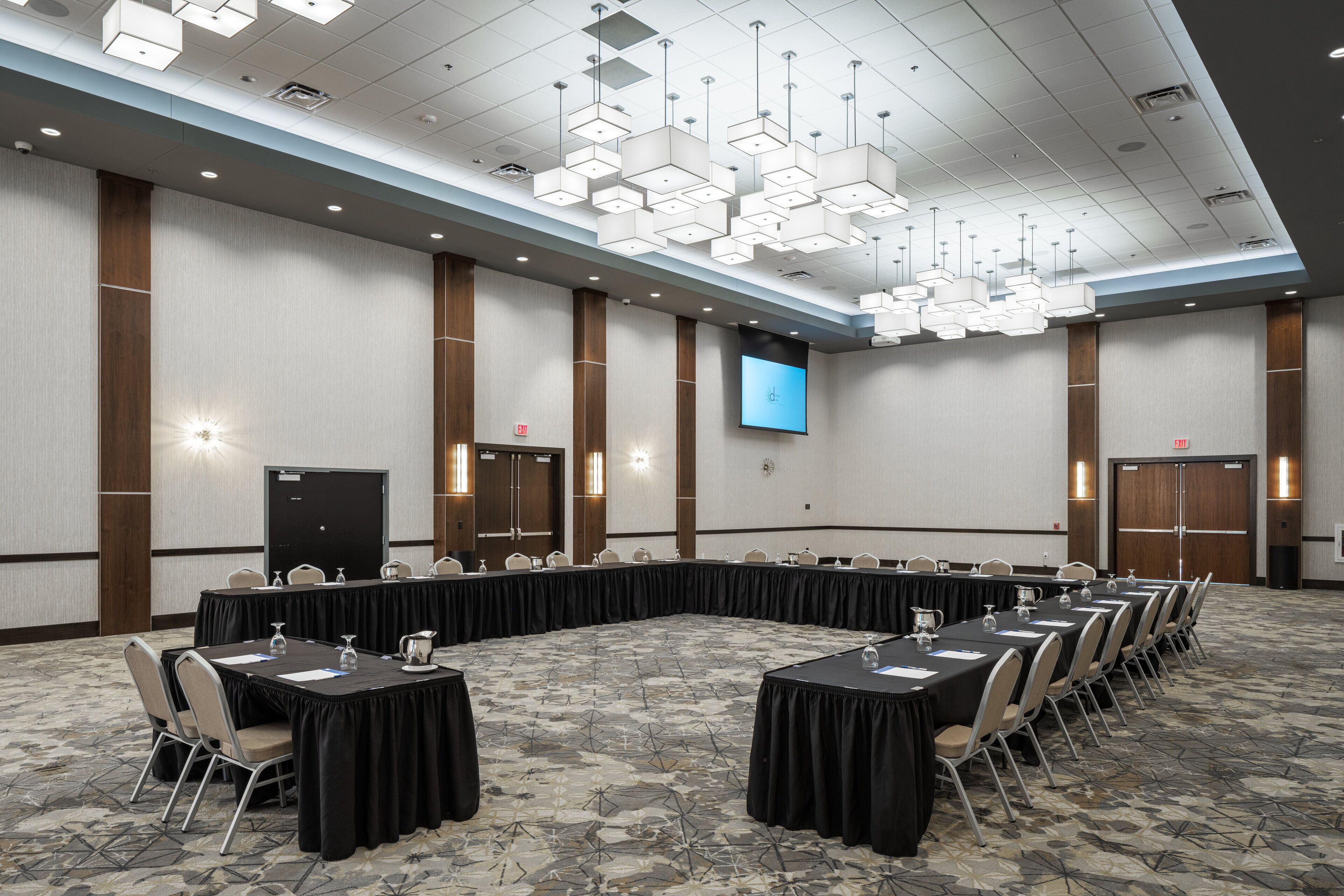 A conference room with a long table, chairs, a screen, and a patterned carpet.