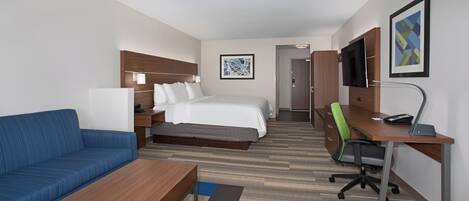 A hotel room with a bed, a blue sofa, a desk with a chair, a TV, and a painting on the wall.