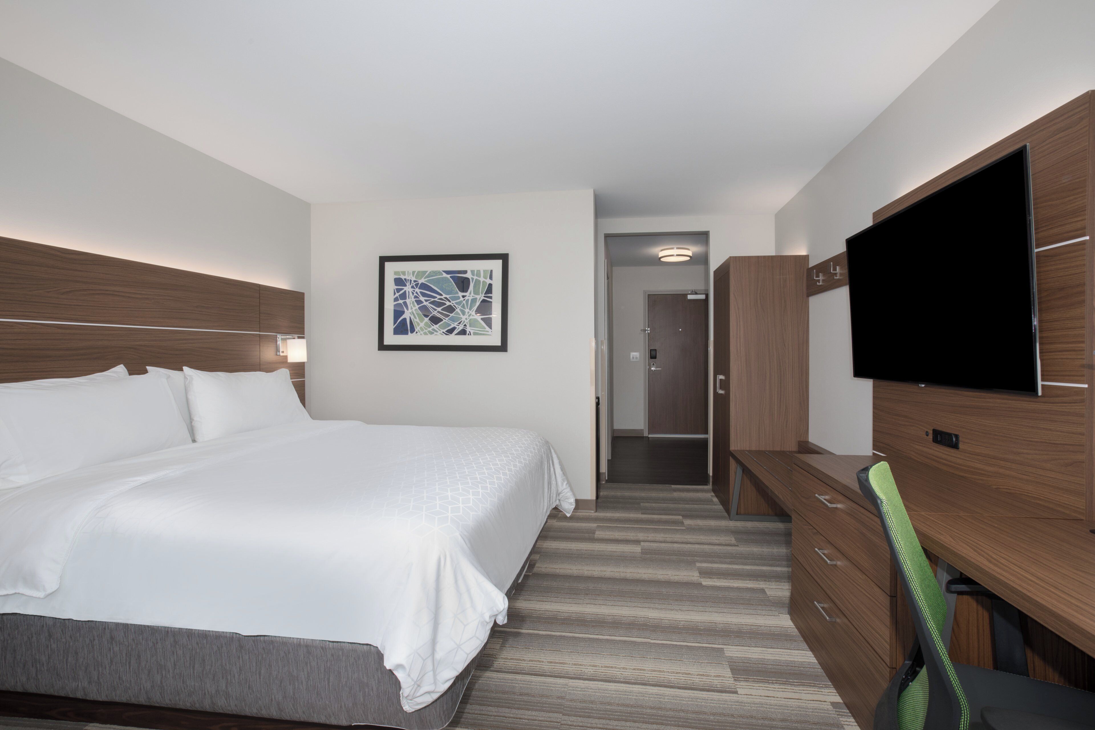 A hotel room with a bed, a desk, a chair, a television, and a door leading to a bathroom.