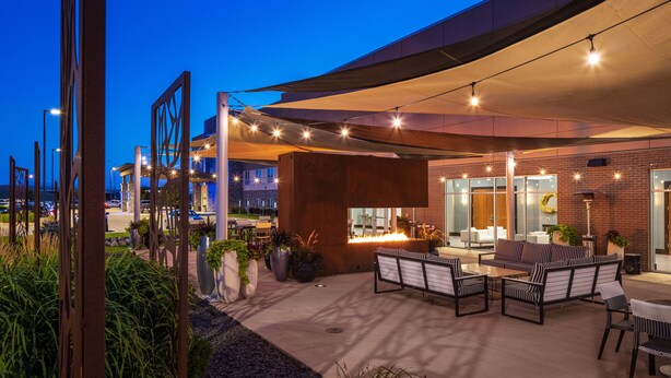 Un espacio al aire libre con patio, mobiliario y una chimenea, rodeado de arquitectura moderna y plantas.