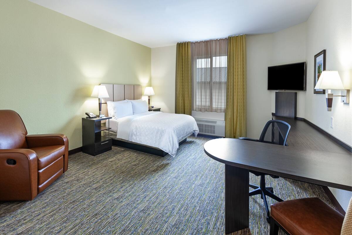 Een hotelkamer met een bed, een bureau, een stoel, een bank, een televisie en een lamp.