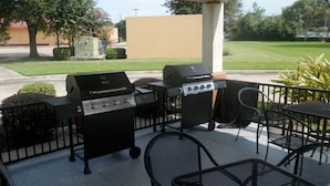 Une terrasse extérieure équipée d’un barbecue et d’un chariot, entourée de chaises et d’une table en métal.