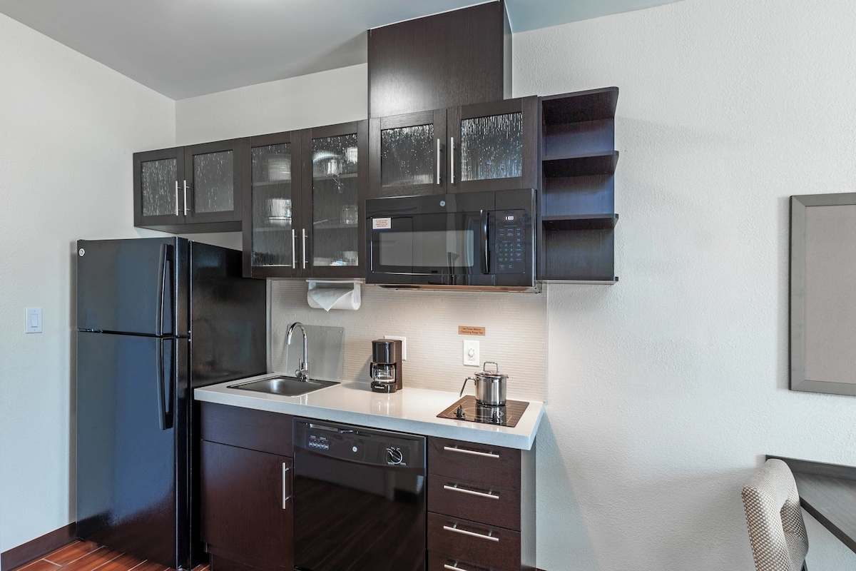 A modern kitchen with dark cabinetry, a stainless steel refrigerator, a microwave, and a coffee maker.