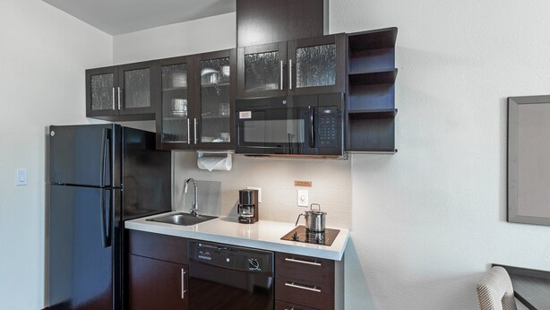 A modern kitchen with dark cabinetry, a stainless steel refrigerator, a microwave, and a coffee maker.
