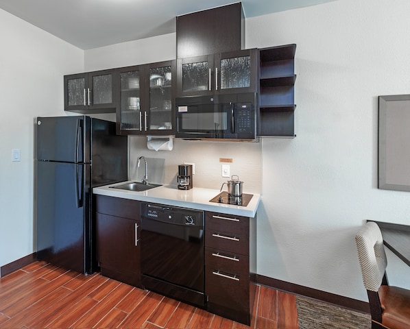 A modern kitchen with dark cabinetry, a stainless steel refrigerator, a microwave, and a coffee maker.