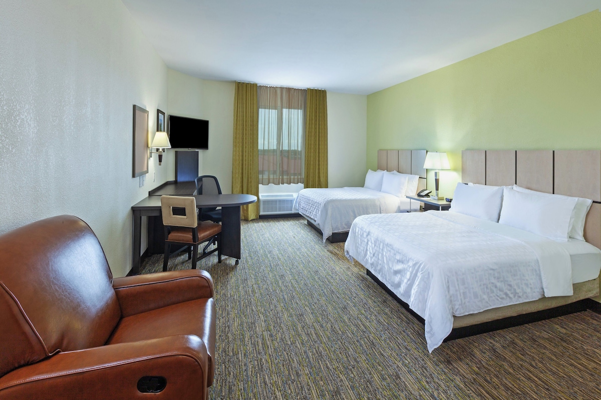 A hotel room with a single bed, a desk with a chair, a sofa, and a television.
