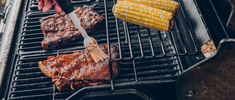 Un barbecue avec de la viande et des épis de maïs.