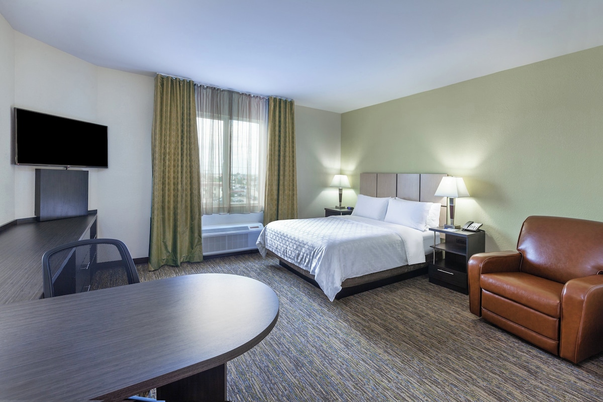 A hotel room with a bed, a desk, a chair, a TV, and a window with curtains.