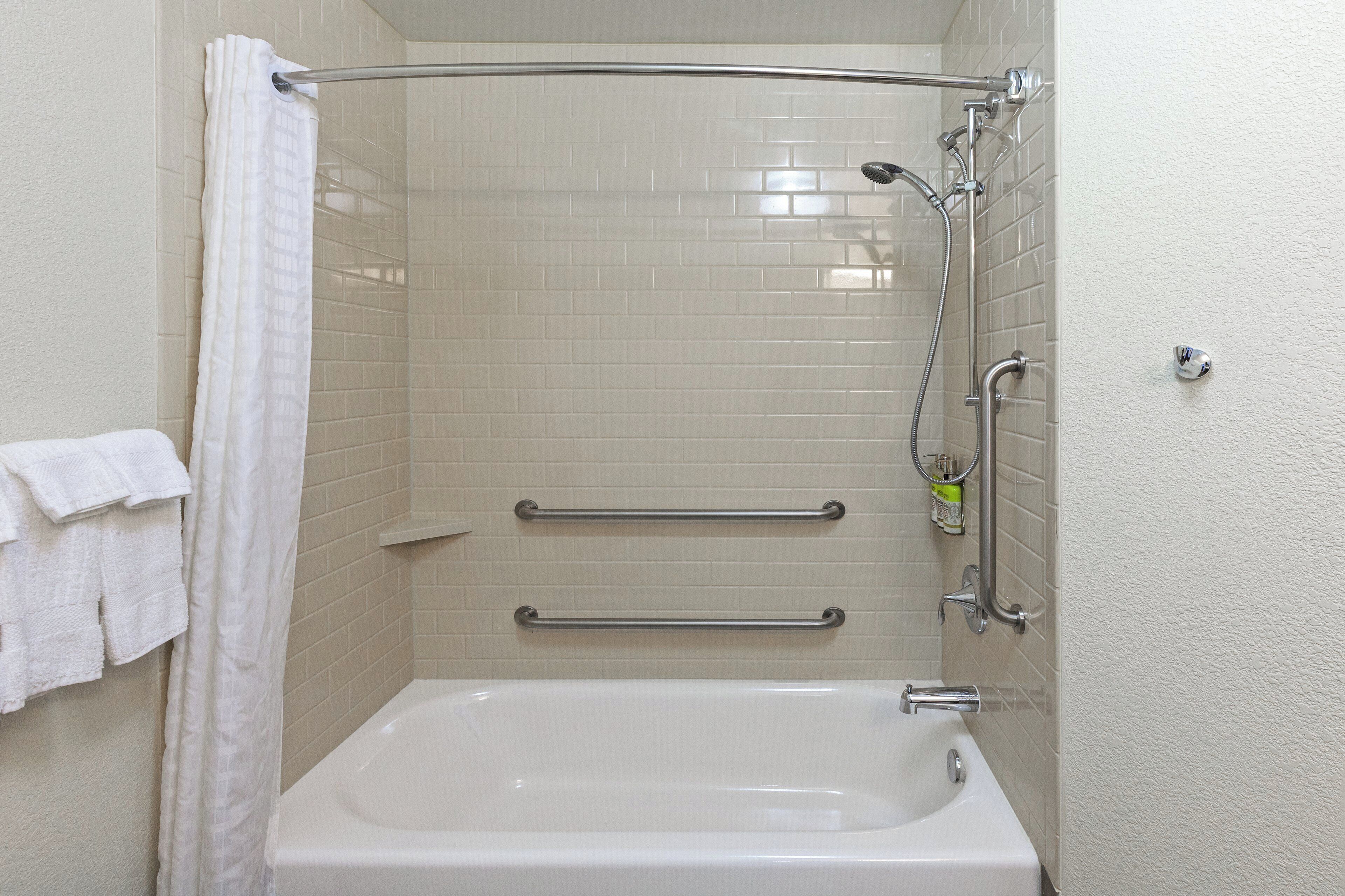 Een badkamer met een wit bad, een douche met een handdouche en twee handgrepen.