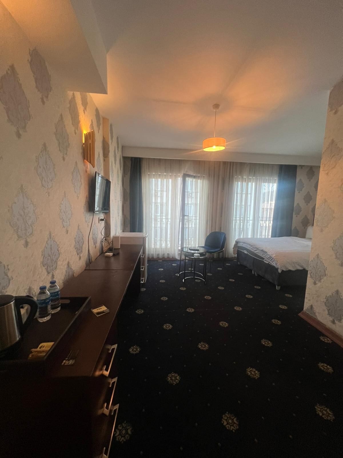 Une chambre d’hôtel avec un lit, un bureau et une chaise, une télévision et une fenêtre avec des rideaux.