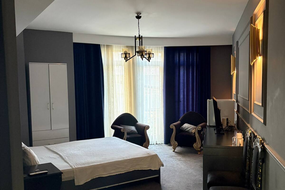 Una habitación de hotel moderna con una cama grande, dos sillones, un escritorio y una araña.