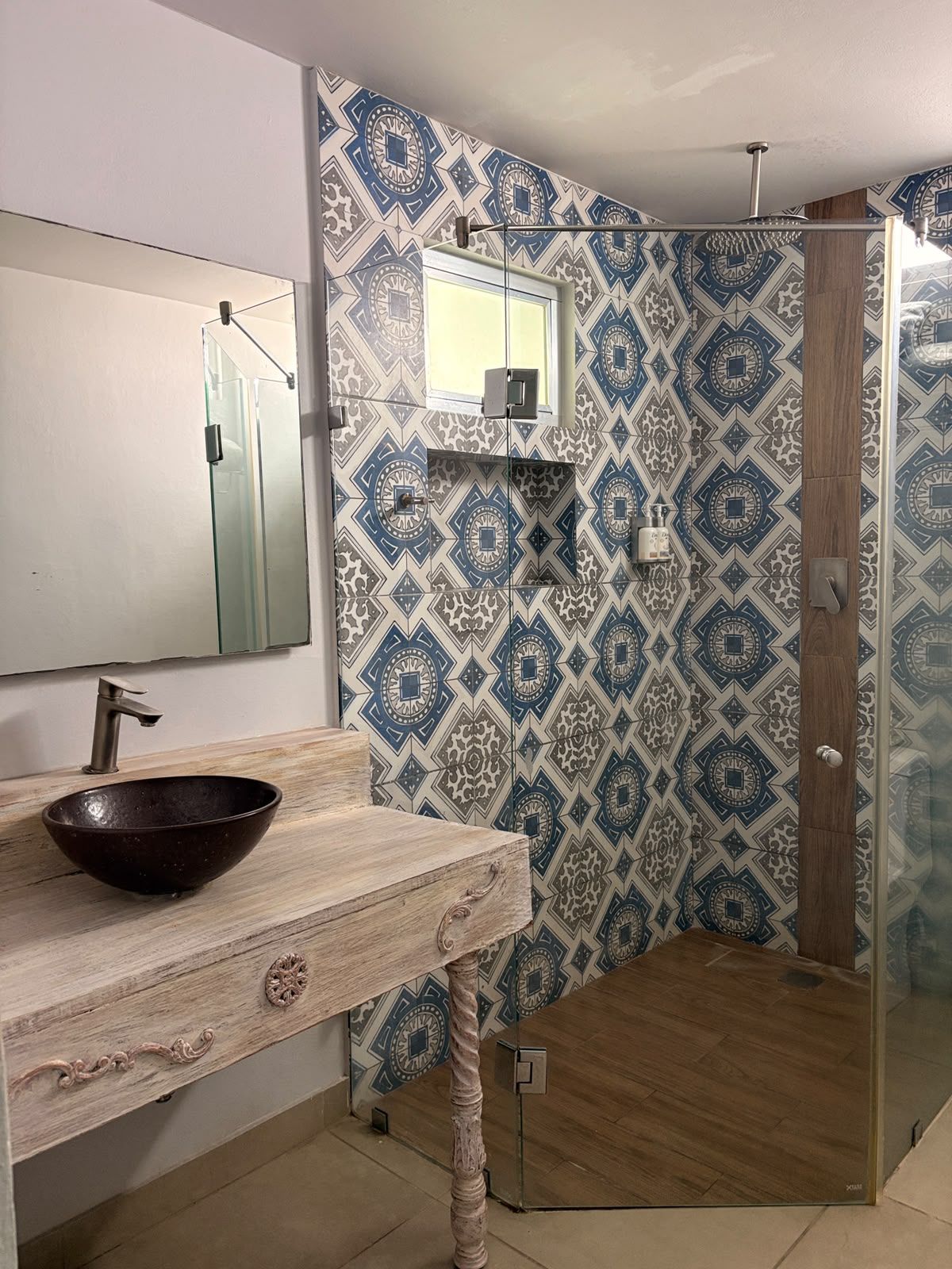 A bathroom with a glass shower enclosure, a wooden vanity with a bowl sink, and patterned tiles on the walls.