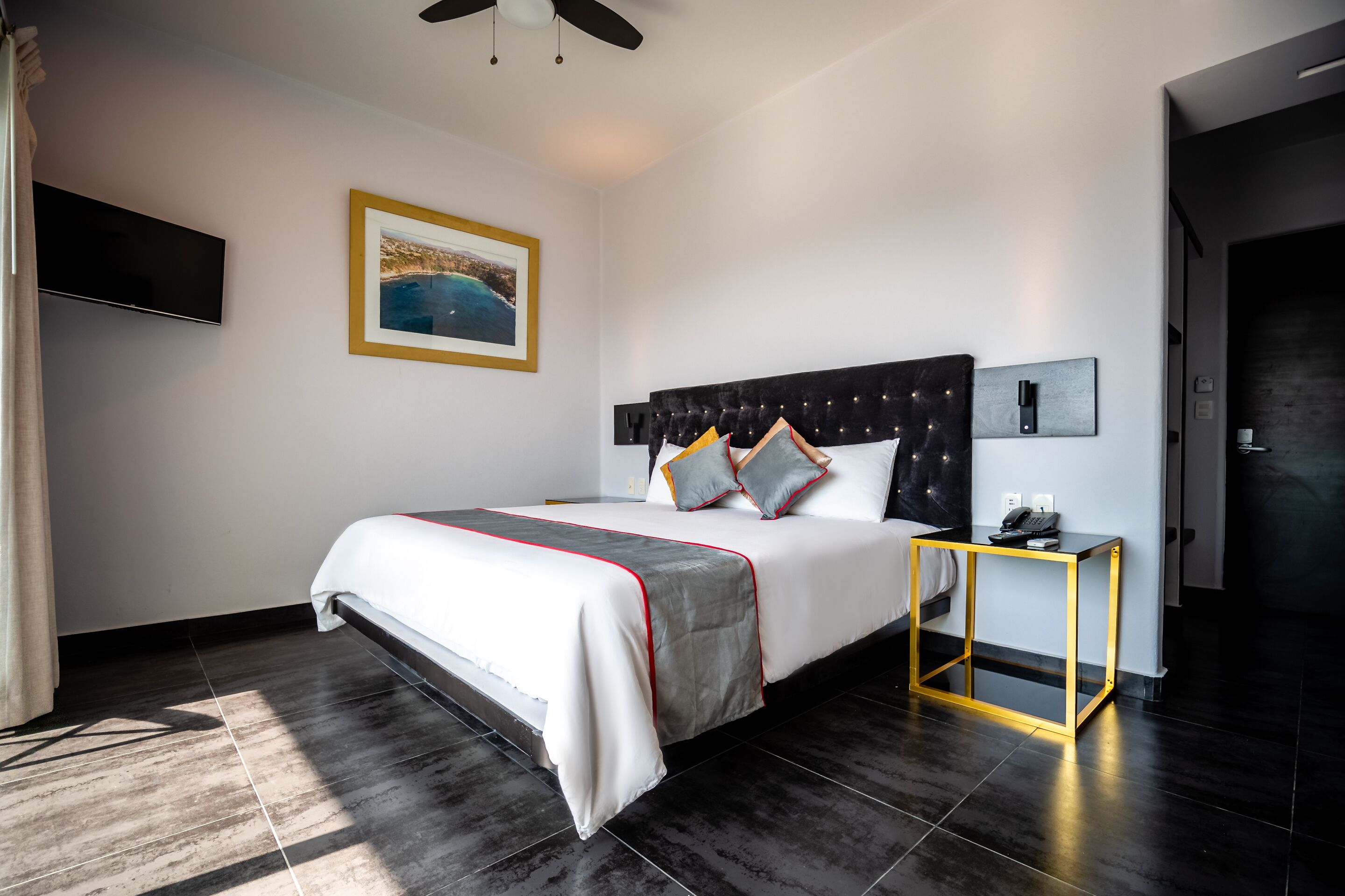 A modern hotel room with a large bed, a flat-screen TV, a framed picture on the wall, and a small table with a phone.