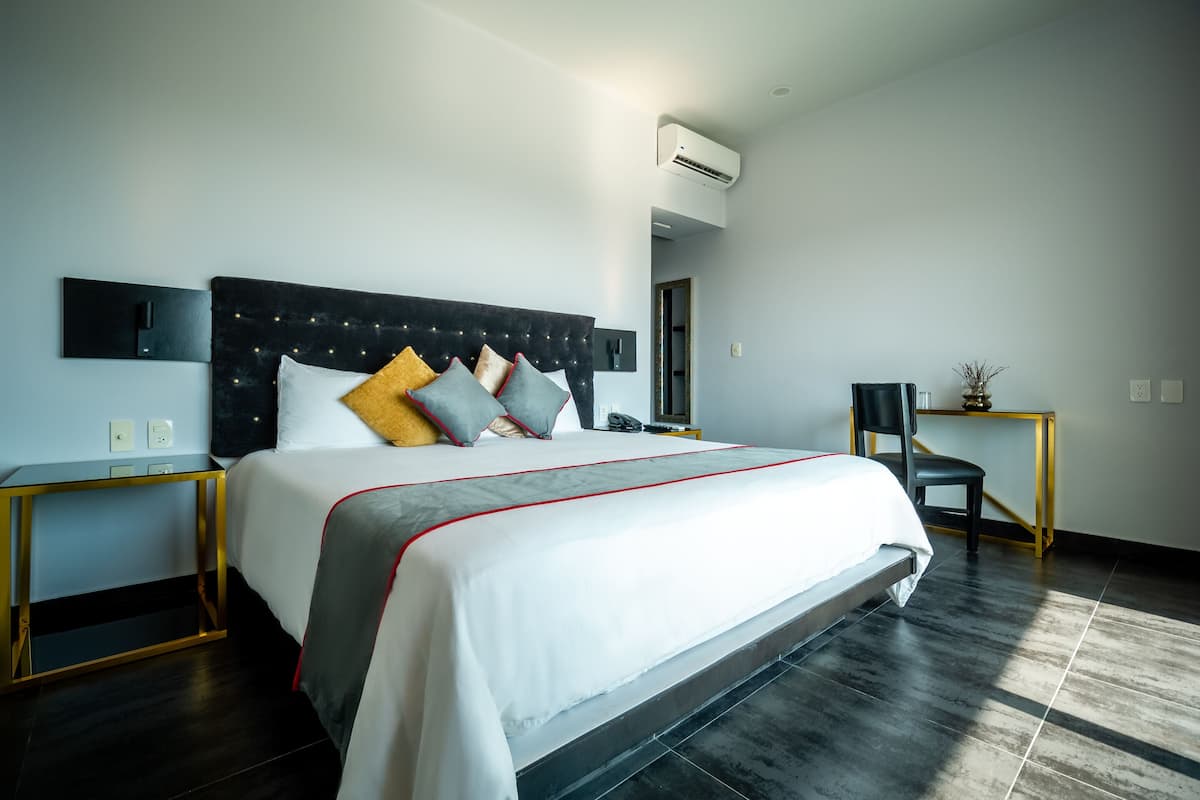 A modern hotel room with a large bed, a bedside table, a chair, and an air conditioning unit.