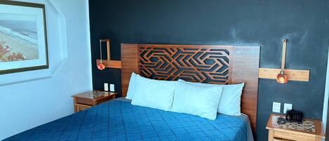 A bedroom with a bed, a nightstand, a wall-mounted lamp, and a framed picture.