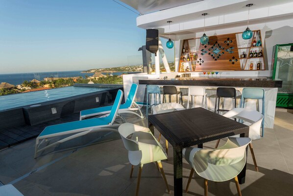 A rooftop bar with a pool view, bar area with shelves, and seating. - Hotel DC Boutique & SPA (Puerto Escondido)