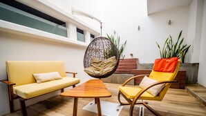 A modern outdoor seating area with a wooden table, a yellow sofa, a hanging chair, and a yellow armchair. - Hotel DC Boutique & SPA (Puerto Escondido)