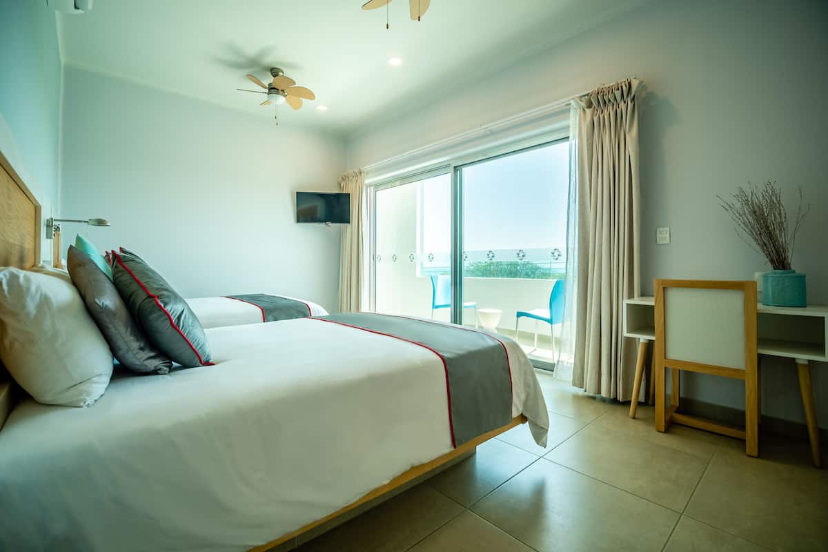A hotel room with a bed, a desk, a chair, a TV, and a balcony with a view.