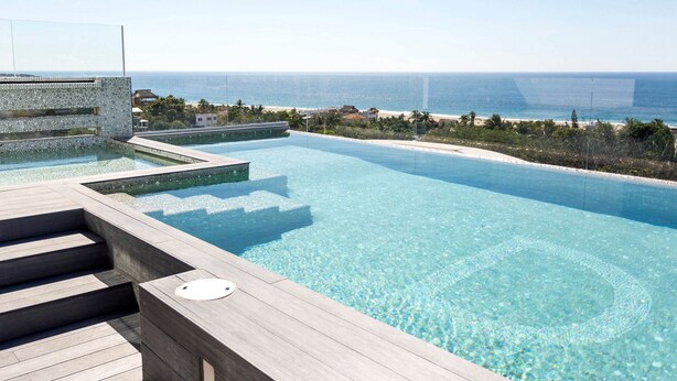 A clear view of a swimming pool with steps leading into it, surrounded by a wooden deck. - Hotel DC Boutique & SPA (Puerto Escondido)