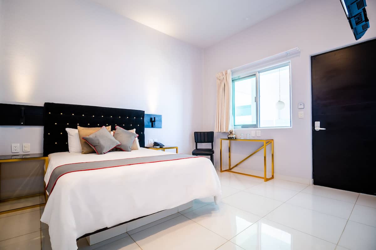 A modern hotel room with a large bed, bedside tables, a desk, and a window with curtains.
