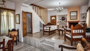 A traditional living room with a wooden staircase, a fireplace, and a dining area with wooden furniture. - Petrinos Milos (Agios Vasileios)