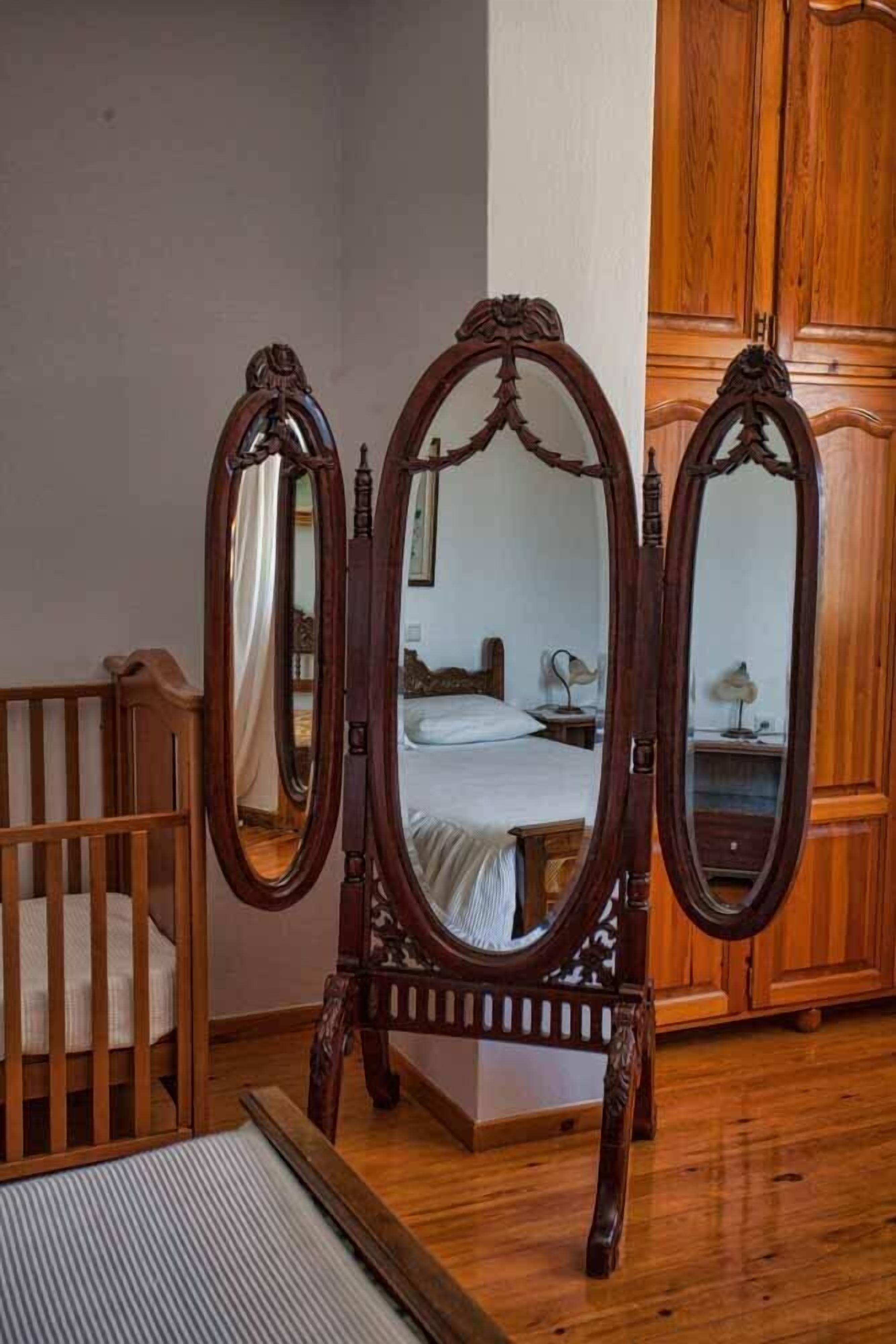 A bedroom with a wooden crib, a bed with a white bedspread, and a wooden wardrobe.