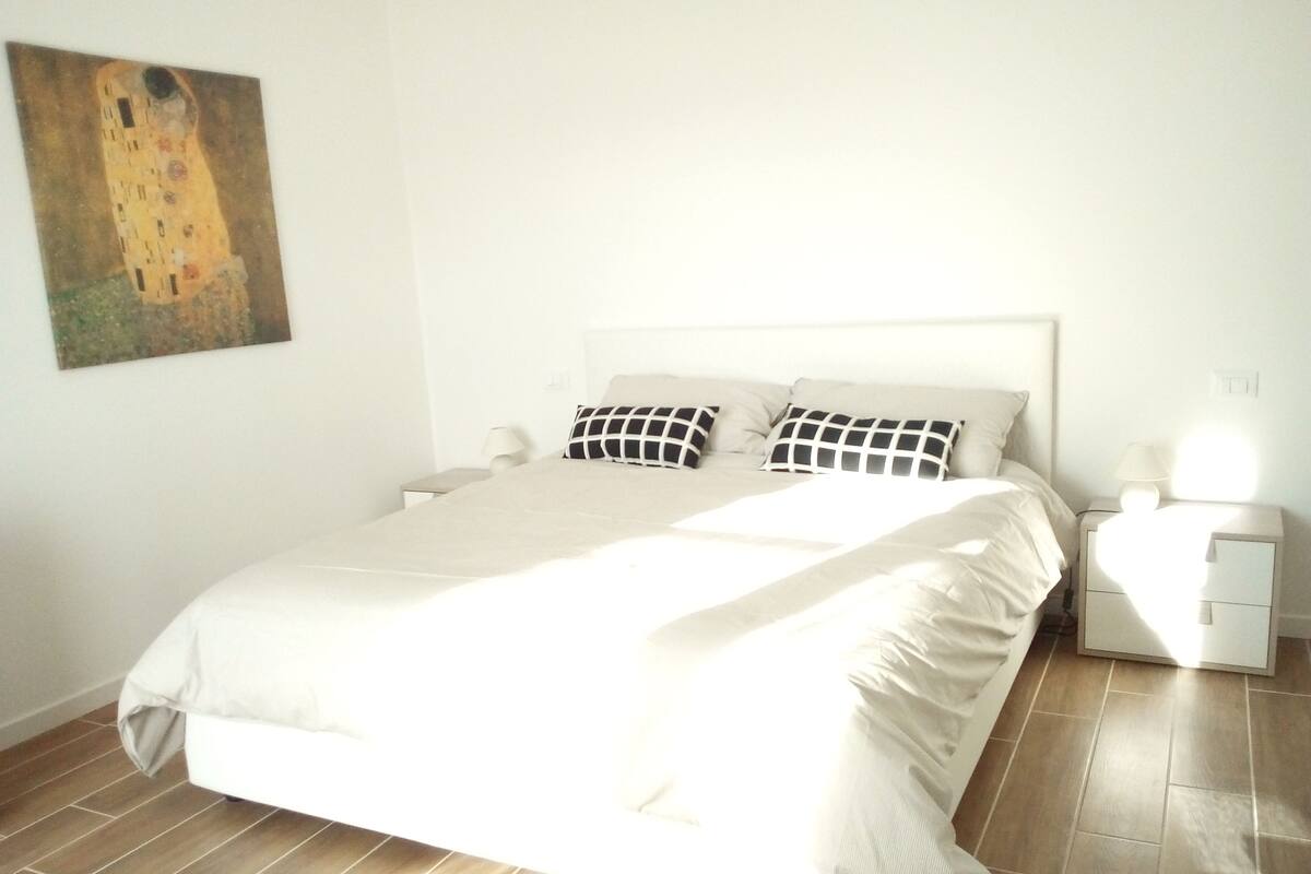A neatly made bed with a white headboard, two bedside tables with lamps, and a painting on the wall.