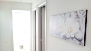 A hallway with a white door at the end, a painting of white flowers on the wall, and a tiled floor. - Bed and Breakfast Bio Salix (Padova)