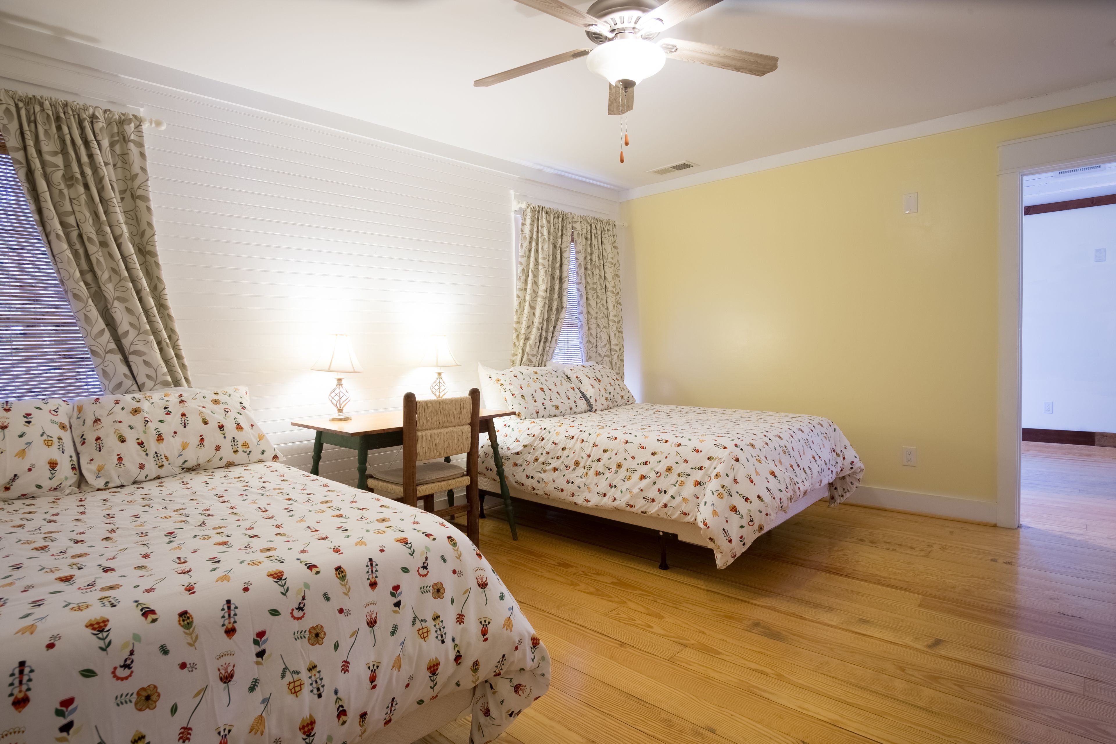 A bedroom with two beds, a ceiling fan, and a wooden floor.