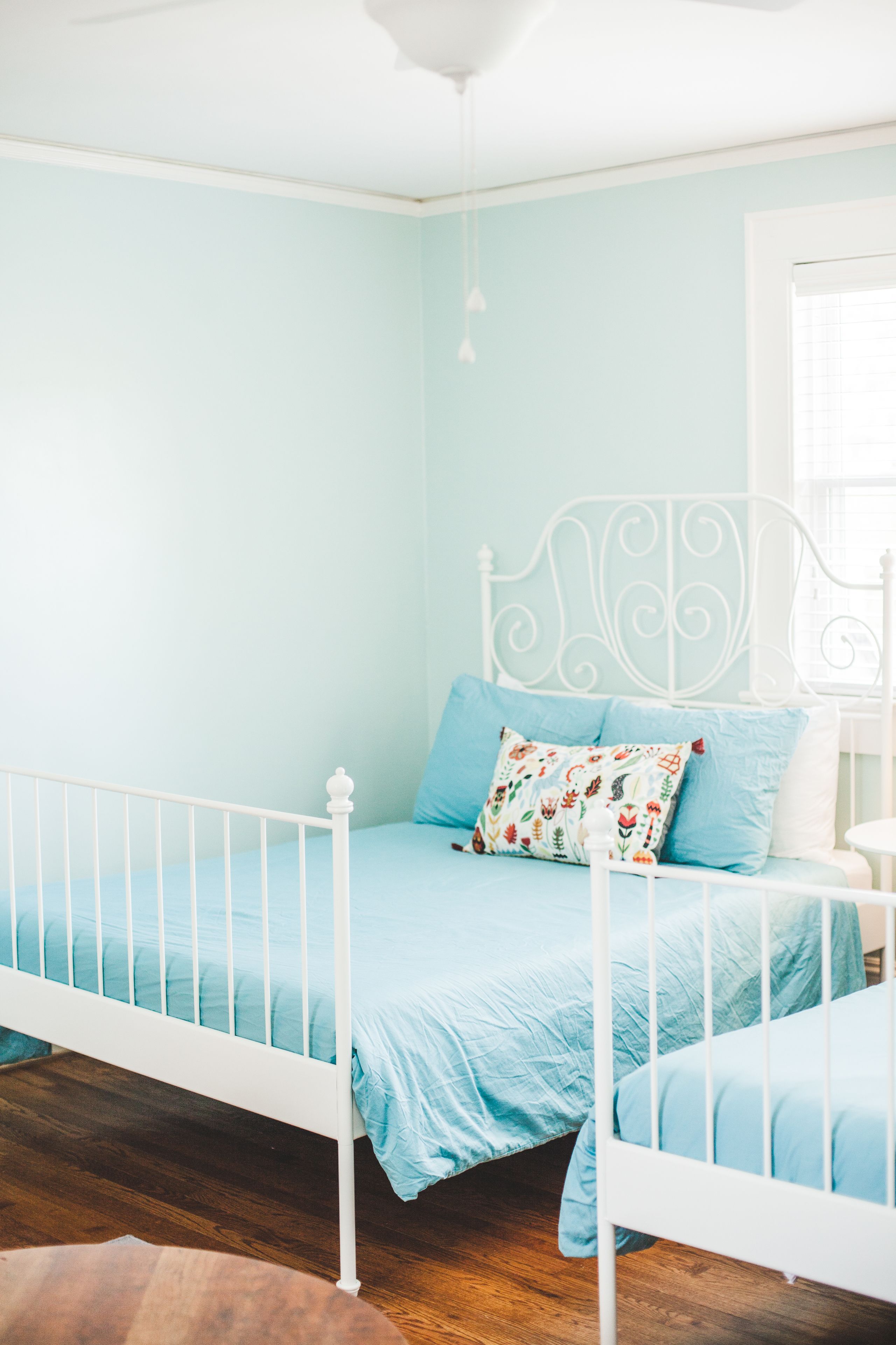 A bedroom with a white metal bed frame, light blue bedding, and a floral pillow.