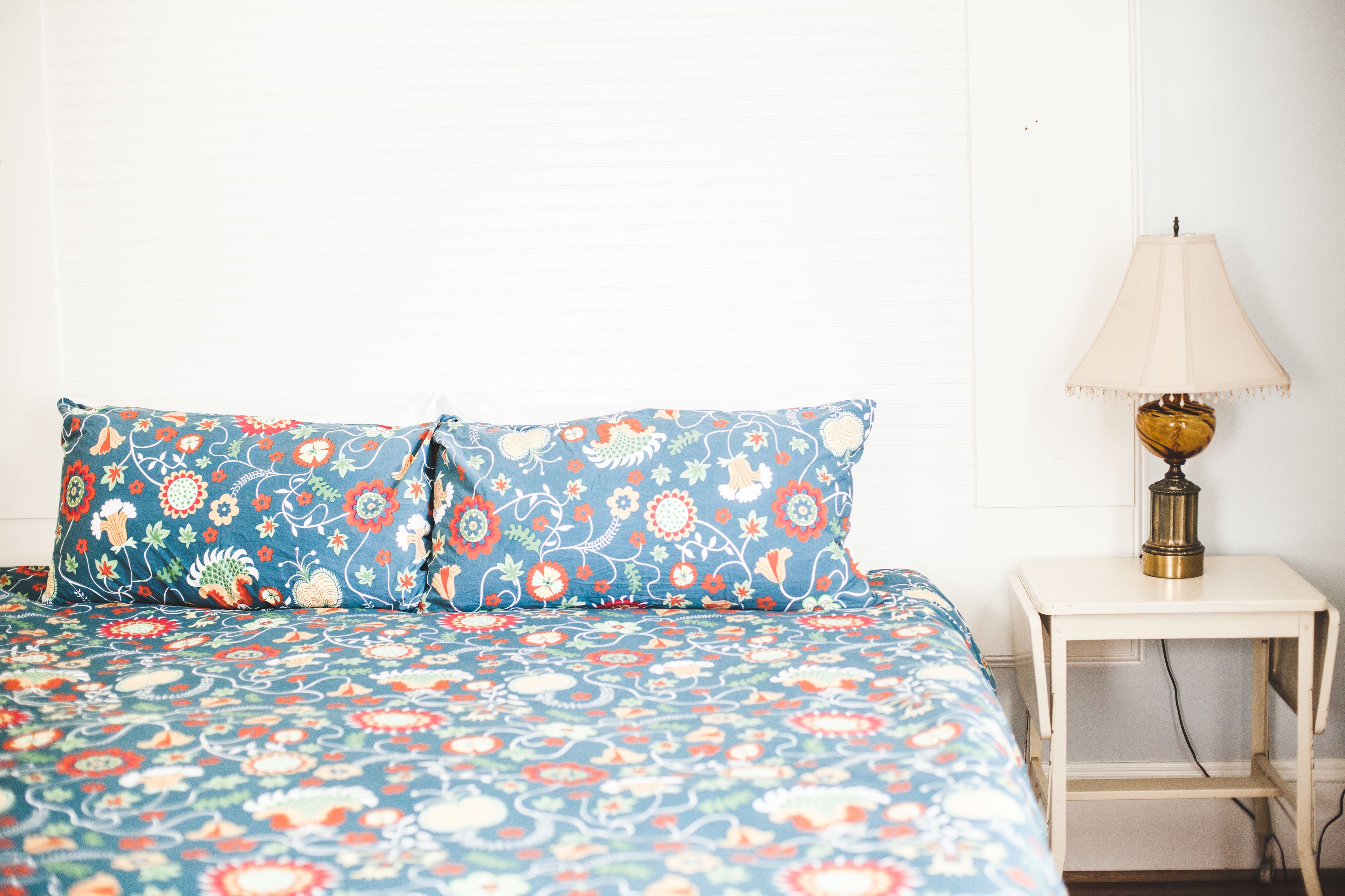 A bed with floral bedding, a bedside lamp, and a white nightstand.