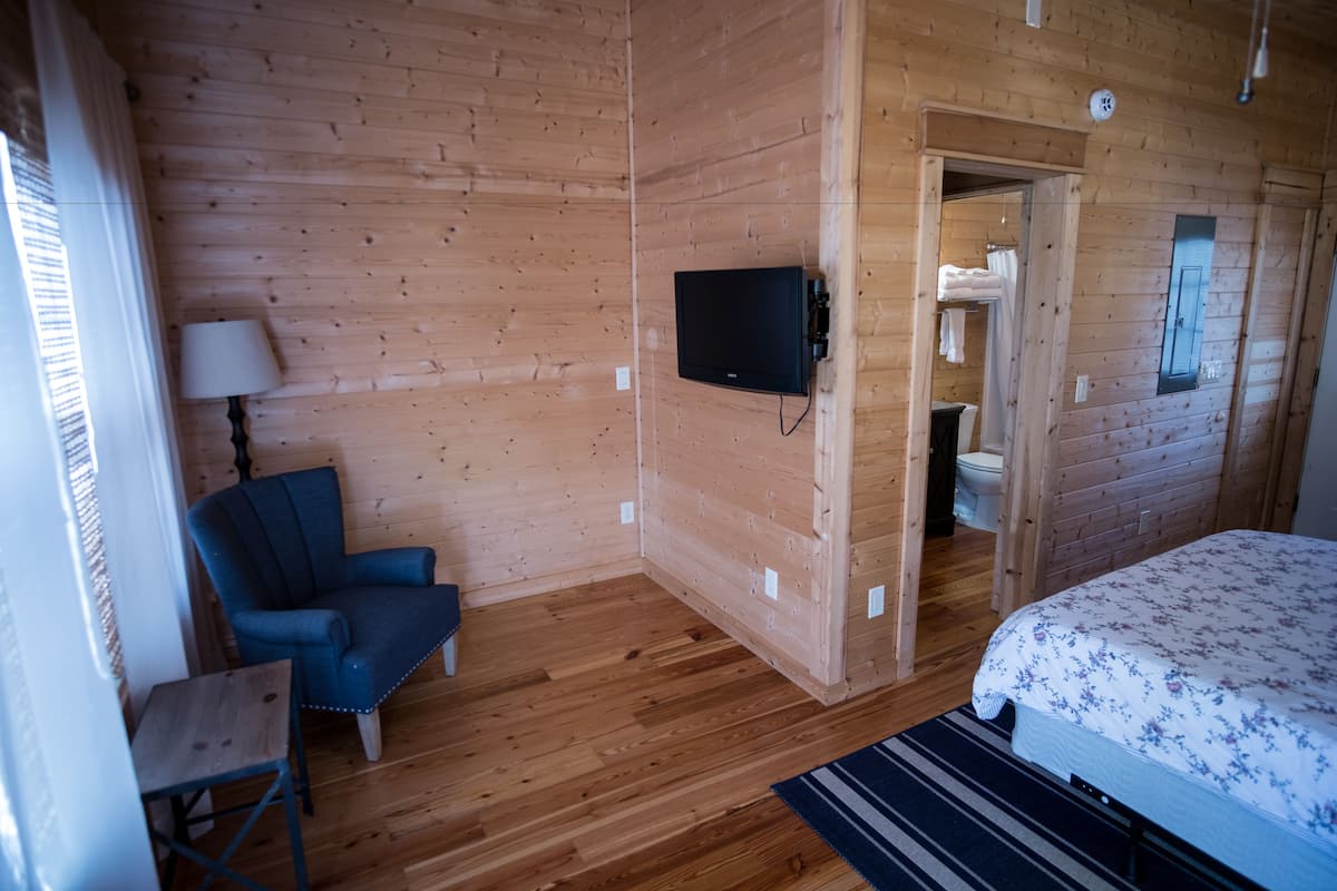 A wooden-paneled room with a bed, a chair, a TV, and a small table.